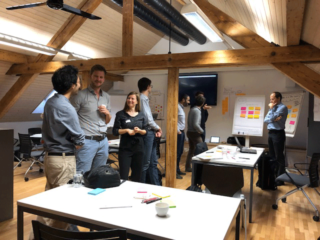 Illustrative photo of the commons space at the ieLab offices with participants standing together and exchanging in conversations over workshop materials.